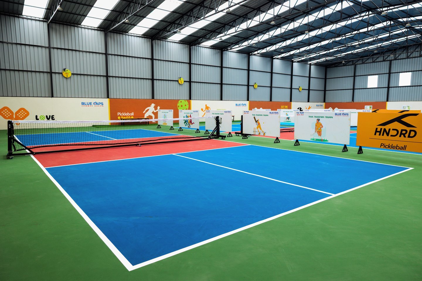 Courts running the length of the arena, with player-graphic panels along the side and an orange HNDRD sign