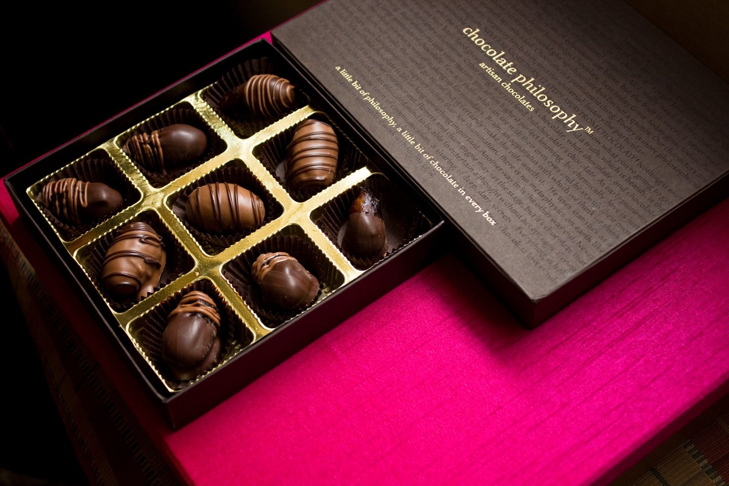 Open Chocolate Philosophy box of striped truffles in a gold tray, resting on a magenta cloth