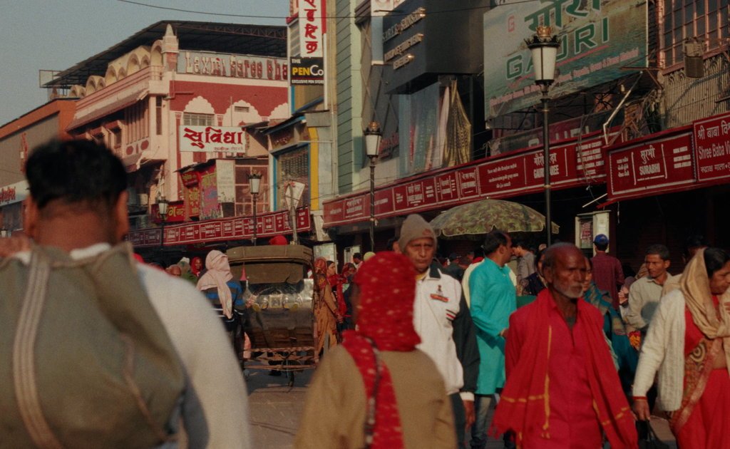 A crowded bazaar street in warm evening light, a man in red in the foreground, from the documentary work