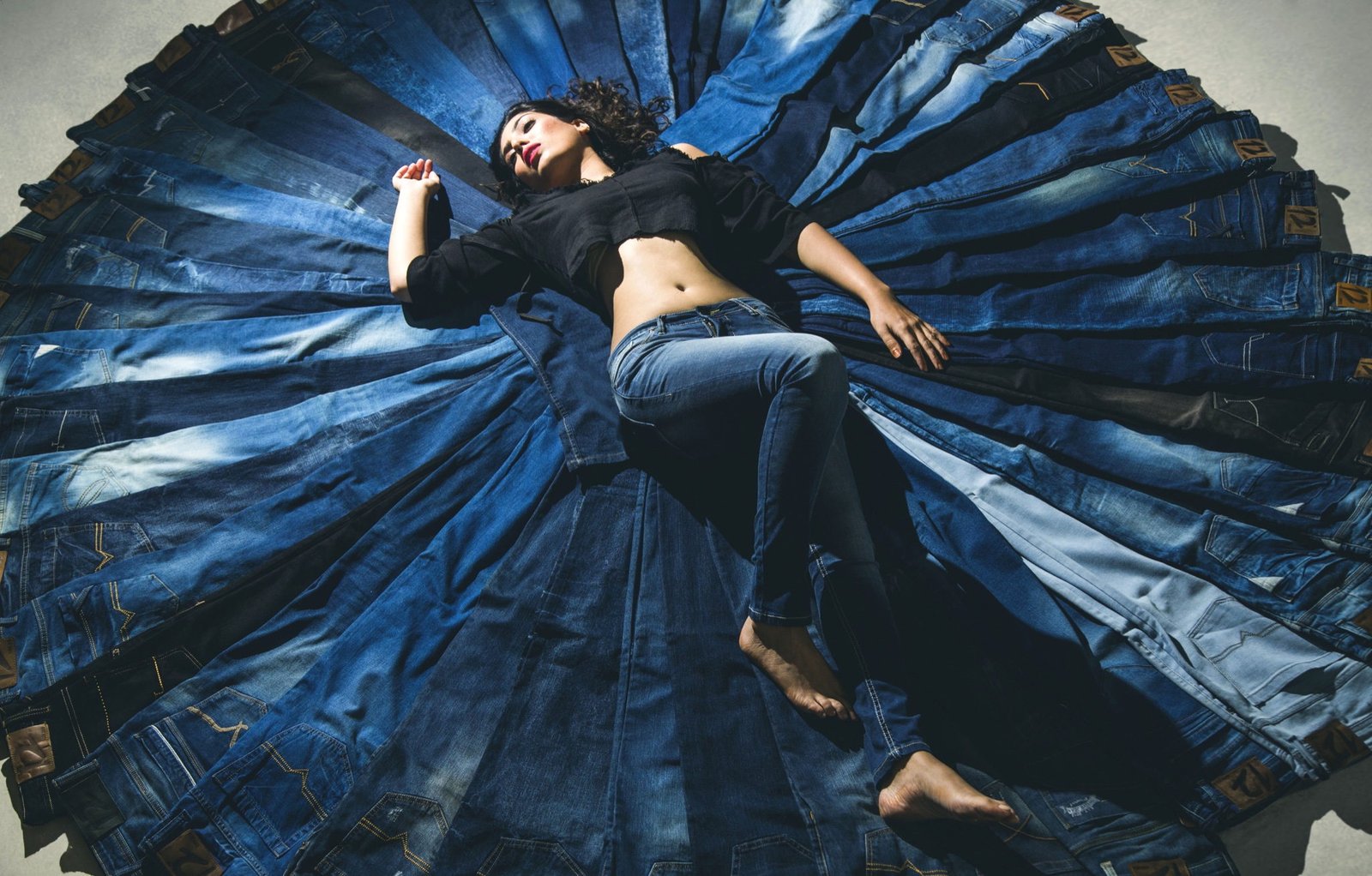 Fashion model reclining at the centre of a circular arrangement of blue jeans