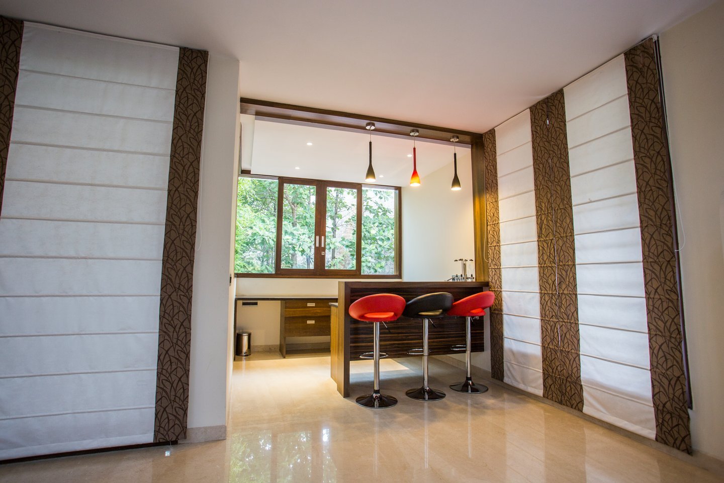 Bar corner with red bar stools, pendant lights and tall roman blinds, looking out to garden windows